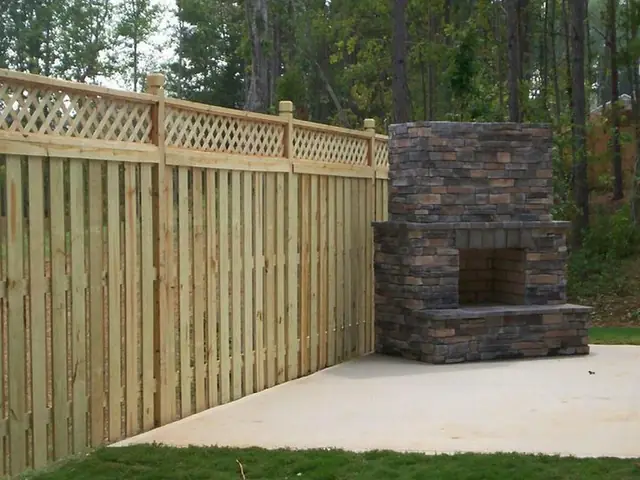 Shadowbox fence with a framed lattice top beside a stone fireplace